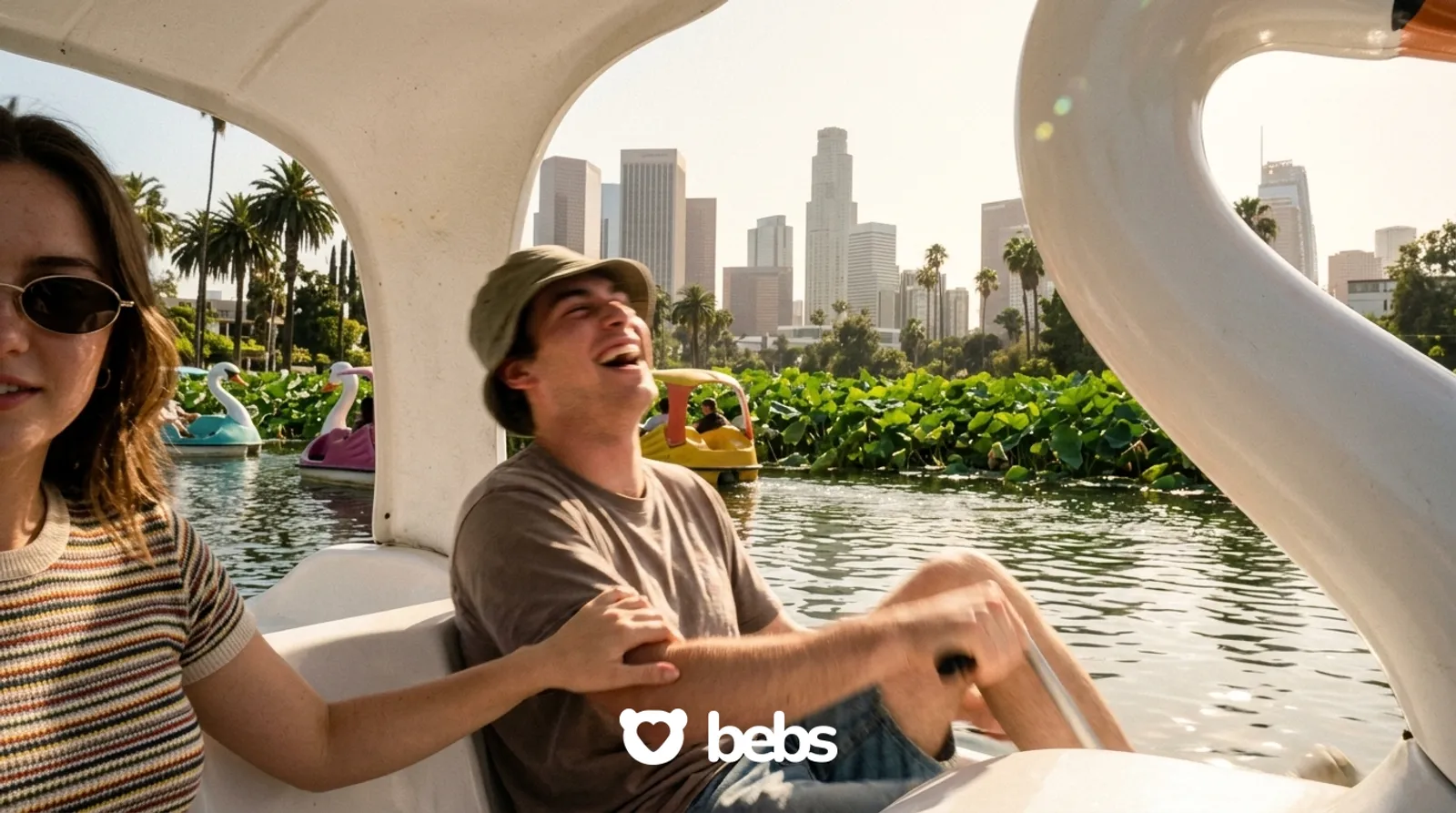 Couple laughing in a swan paddle boat on Echo Park Lake with the downtown LA skyline, a fun and cheap first date idea in Los Angeles